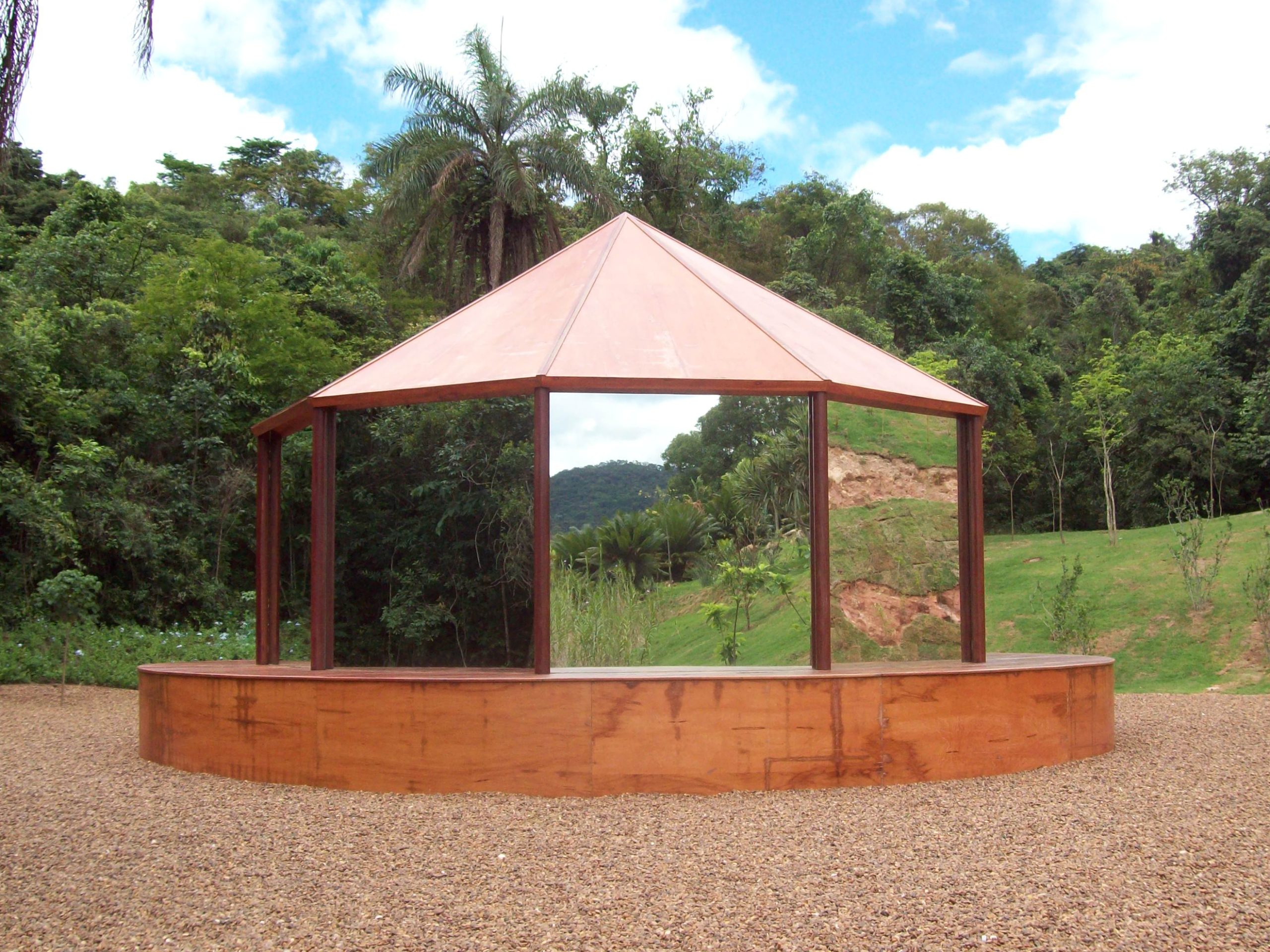 Folly, de perto, uma arquitetura octagonal revestida de espelhos que refletem a vegetação ao redor, com telhado de madeira