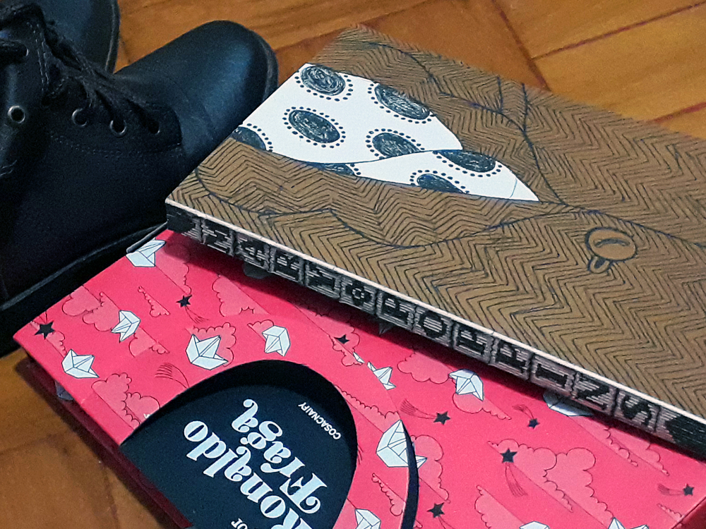Mary Poppins: Foto do livro Mary Poppins, publicado pela editora Cosac Naify, cuja capa simula a roupa da parte superior do corpo da personagem, ou seja, uma camisa de com estampa de bolinhas com um casaco listrado por cima, e lombada branca onde se lê o título da obra em letras grandes e escrito na vertical. O livro está sobre sua luva, que simula a maleta usada pela personagem. Ao lado há um par de botas de cor escura.