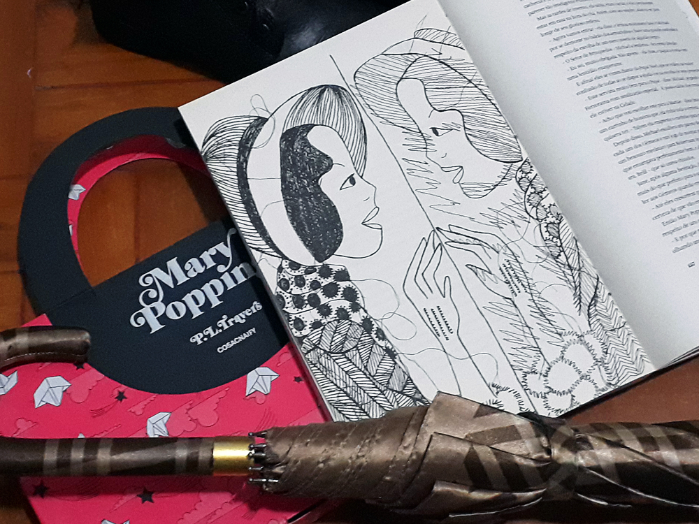 Mary Poppins: Foto do livro Mary Poppins, publicado pela editora Cosac Naify, aaberta em uma página onde se vê uma ilustração da personagem protagonista se olhando no espelho. O livro está sobre sua luva, que simula a maleta usada pela personagem. Abaixo há um guarda chuvas fechado.
