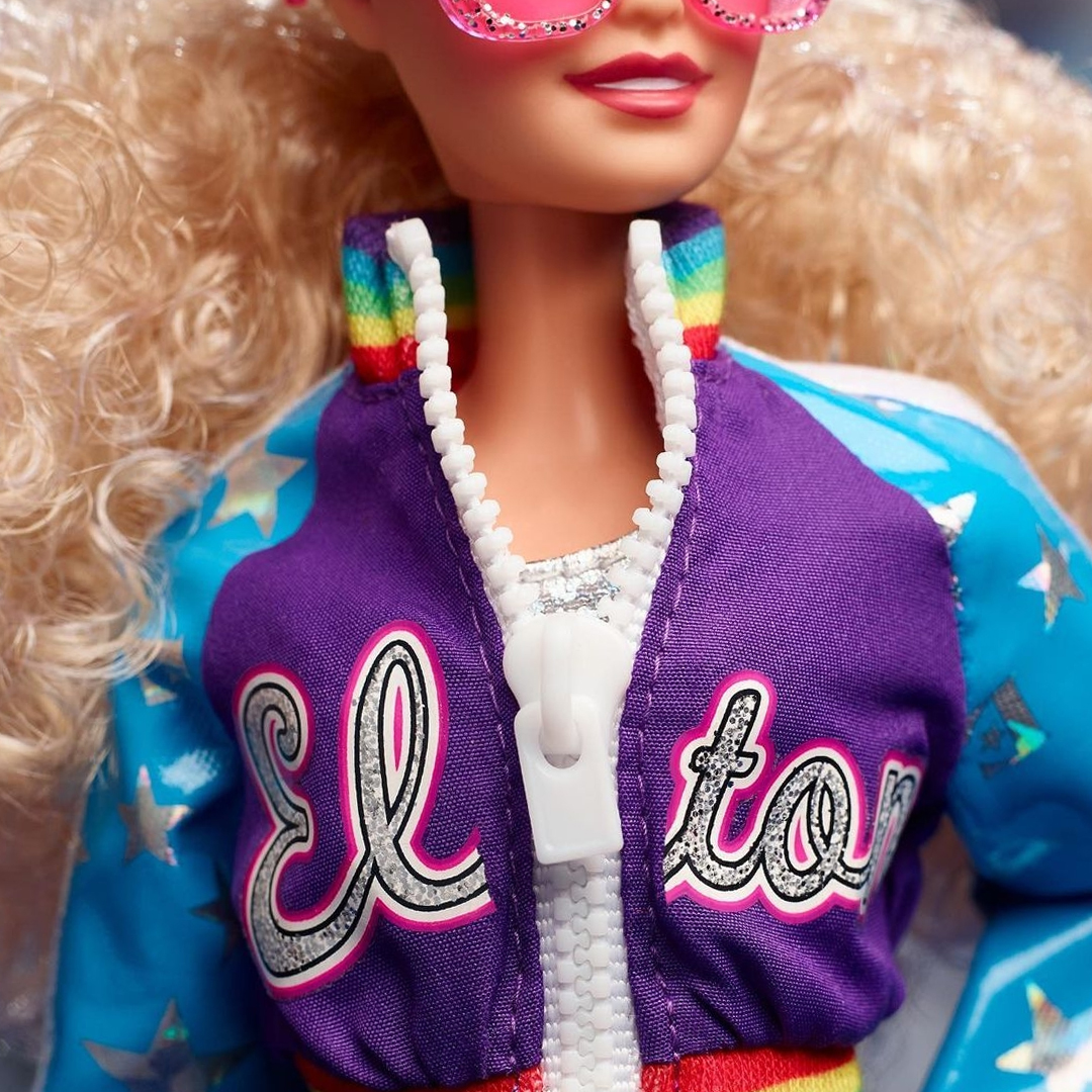 Barbie Elton John: detalhe da jaqueta de zíper onde se lê ''Elton'' bordado na frente, e da camiseta simples e brilhante por baixo.