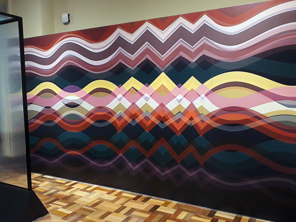 Painel de Abraham Palatnik composto de linhas de diversas cores e espessuras formando, ao mesmo tempo, zig-zags e ondas, causando ilusão de ótica ao expectador.