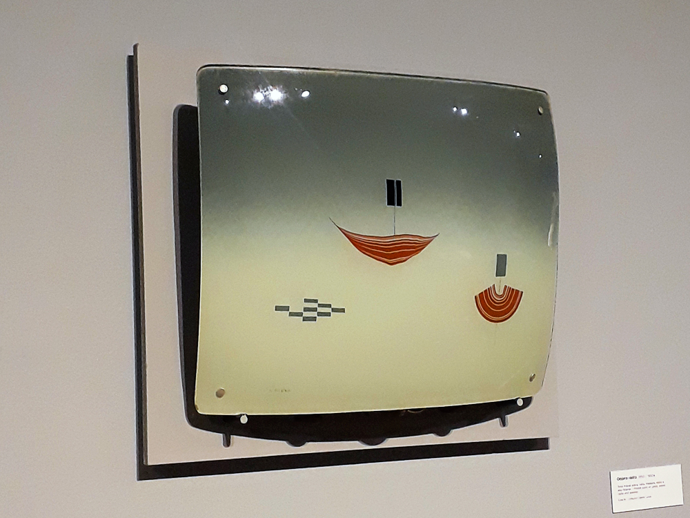 Pintura em vidro, que cria relevo em relação ao fundo de cor neutra, com fundo em degradê neutro e imagens abstratas de cores alegras no sempre, podendo representar barcos a vela (pela interpretação da visitante).
