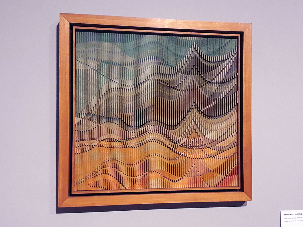 Quadro feito de ripas de madeira organizados em baixo e alto relevos, pintados  de forma que a tinta ajude no efeito de ondas e picos formado na tela.