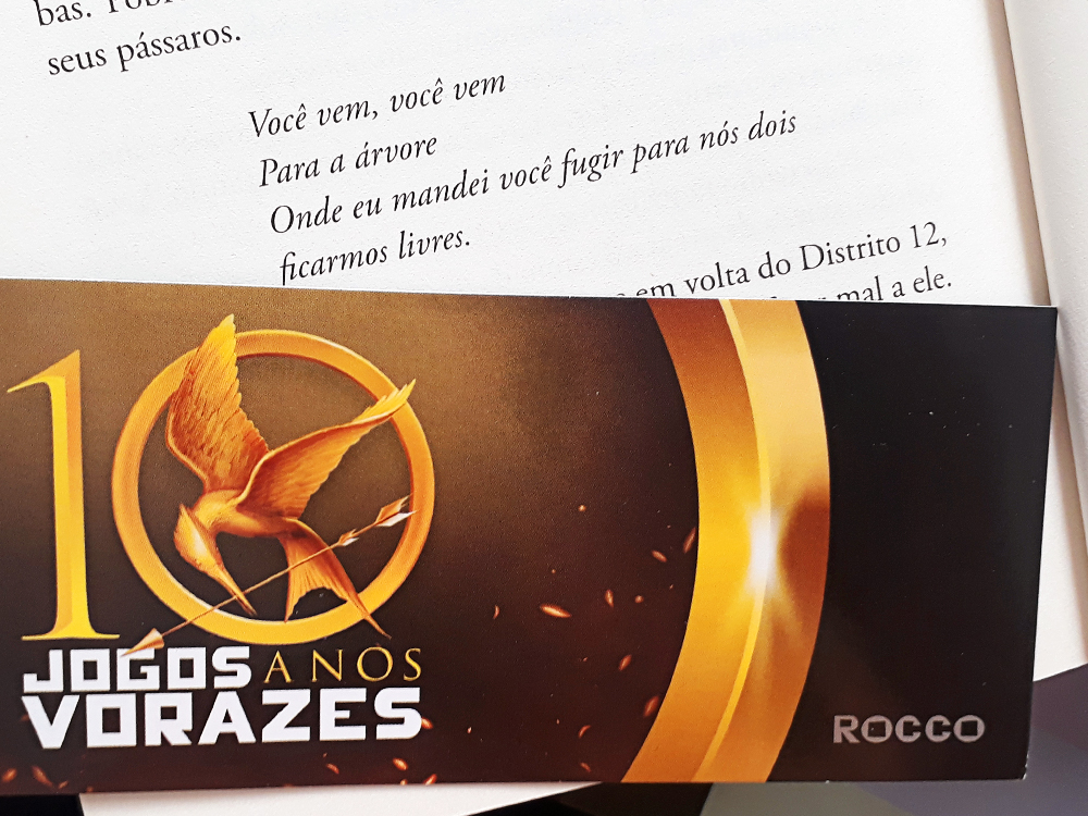 Citação da música 'A Árvore Forca' presente no livro, com o marcador comemorativo dos 10 anos de Jogos Vorazes em baixo.