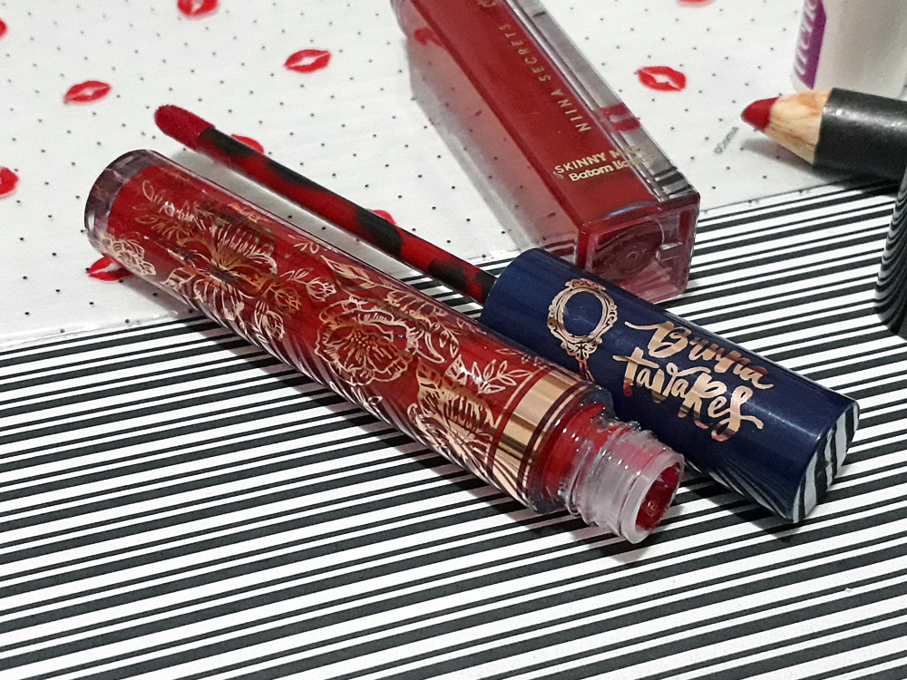 Batom Bruna, da marca linha Bruna Tavares, colocado aberto deitado sobre uma superfície plana de estampas variadas.