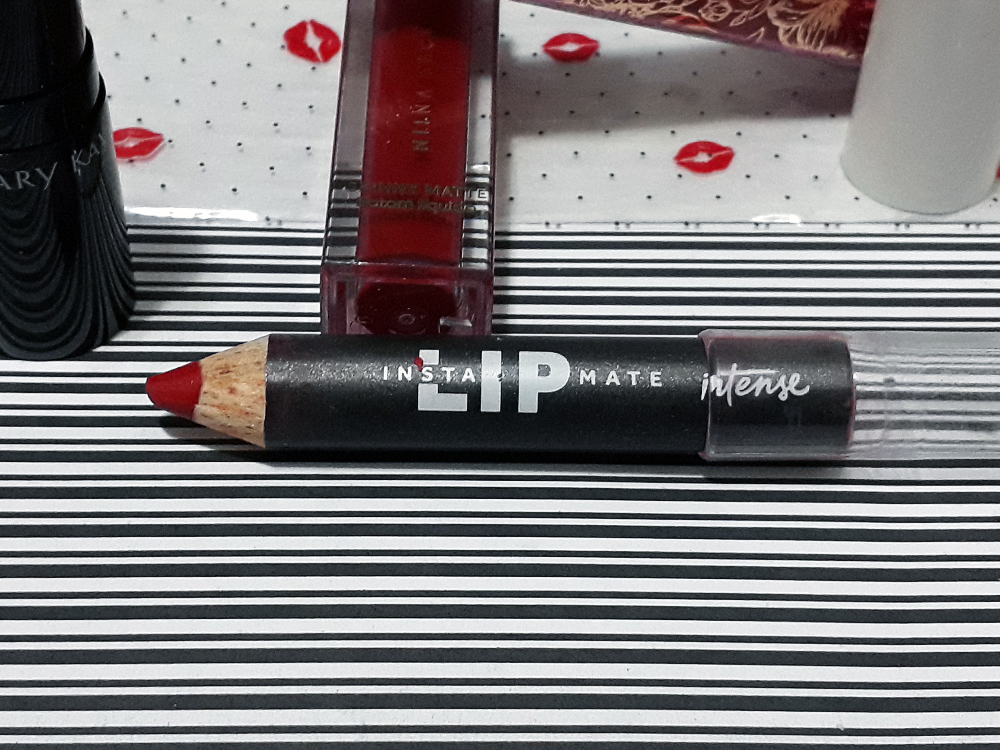 Lápis batom Vermelho  da linha Intense de O Boticário, aberto e deitado sobre as mesma superfície plana estampada das outras fotos.