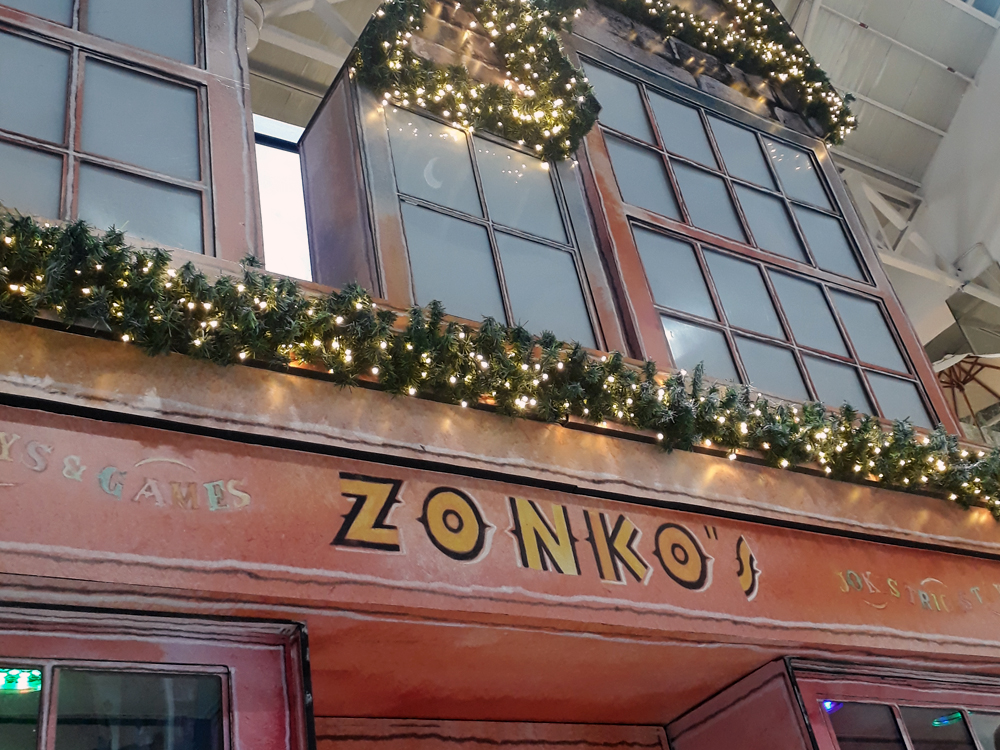 Detalhe da fachada da Zonko's, que tem cor avermelhada com o nome da loja e janelas acima da porta.
