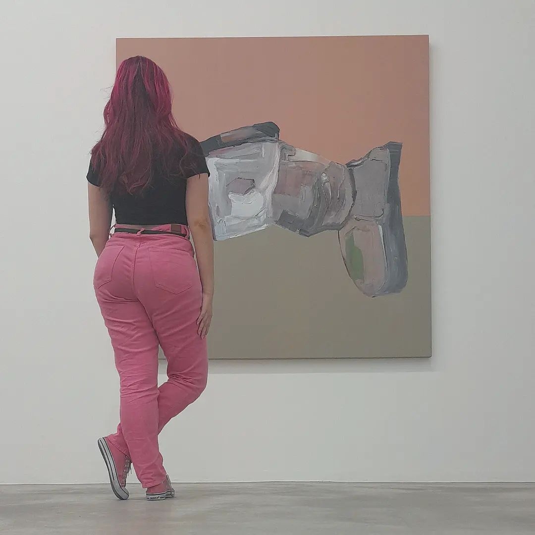 Foto de costas para a câmera, em pé, olhando para um quadro abstrato que se encontra ao fundo