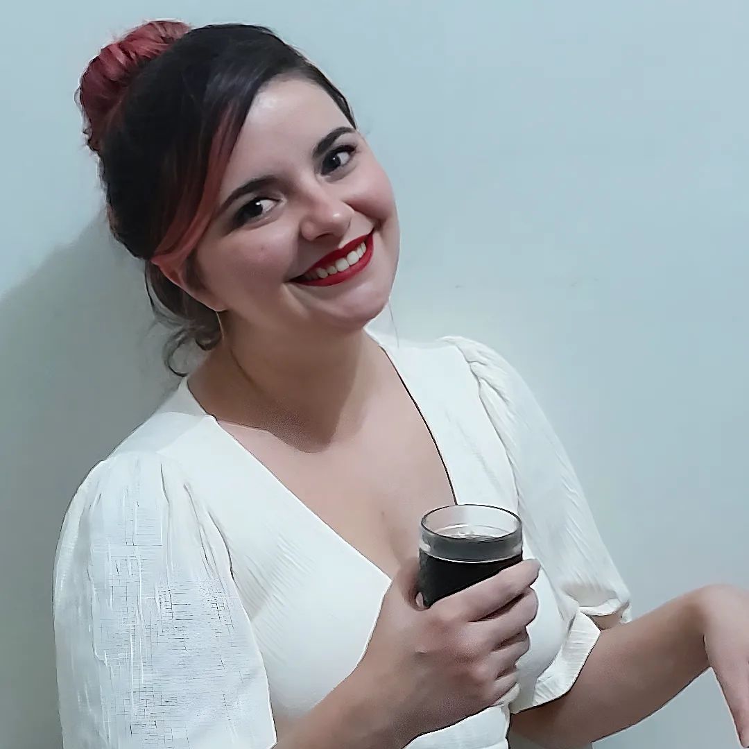 Foto de ano novo de Luly Lage sorrindo usando um vestido branco, cabelos presos em um coque e segurando um copo de Coca-Cola
