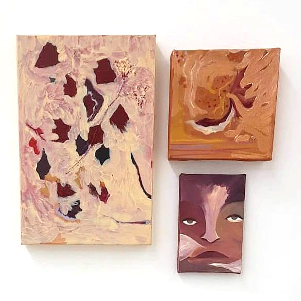 Conjunto de três pinturas instaladas lado a lado: à esquerda, tela abstrata em tons rosados e creme com manchas escuras; à direita, composição em laranja terroso com formas fluidas; abaixo, retrato estilizado de um rosto feminino com olhar voltado para cima.