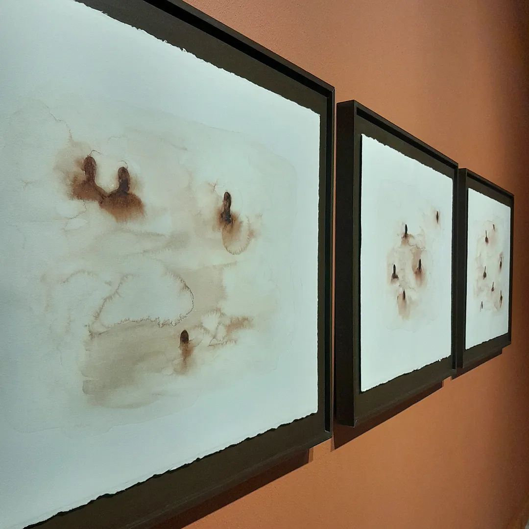 Três pinturas em aquarela, representando fundo aguado e pequenos vultos de pessoas por cima, tudo em tom amarronzado simulando terra molhada.