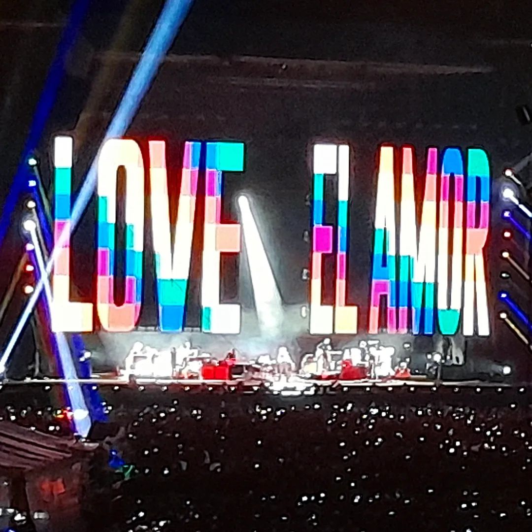 Momento do show onde a palavra AMOR aparece ao telão em diversas línguas, com as cores do arco-íris.