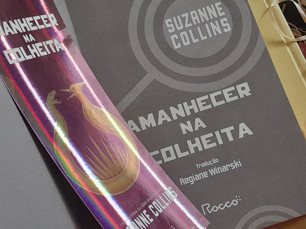 Folha de rosto cinza escuro, contendo nome da autora, título, editora e tradução. Ao sue lado, um marcador roxo e metalizado temático do livro.