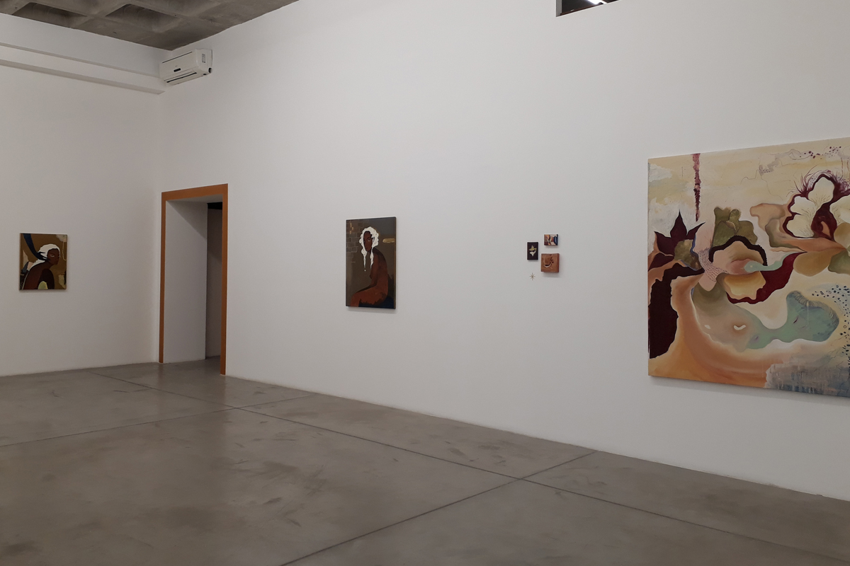 Vista da exposição onde é possível ver várias pinturas, entre abstratas e figurativas, e um portal com as bordas douradas ao fundo.