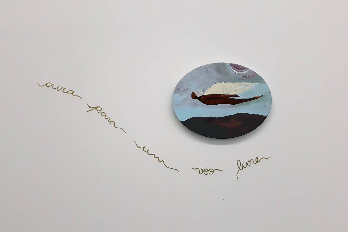 Pintura Meu voo livre de Jess Vieira, em formato oval horizontal, onde a pessoa retratada possui asas brancas e voa deitada com um céu azul ao fundo. Na parede, em torno da pintura, a artista escreveu em dourado FUGA PARA UM VOO LIVRE.