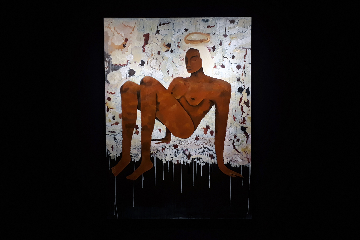 Pintura A sagrada sabedoria que transmuta os sonhos ou Formas de manter o equilíbrio, enquanto eu brinco de viver, de Jess Vieira, em uma parede de cor azul marinho como a parte de baixo da imagem. Ela retrata uma mulher negra de cabelos brancos, nua, de olhos fechados deitada de costas, apoiada pelas mão e pés.