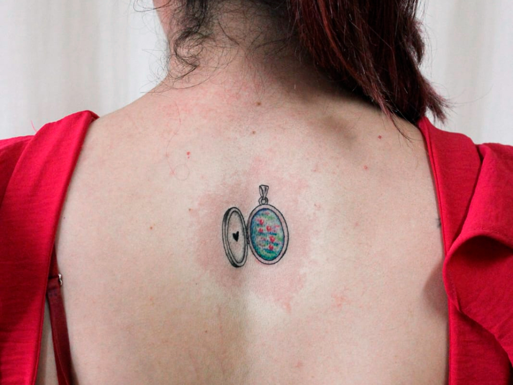 A segunda das duas tatuagens é um relicário aberto no centro das costas. Na parte interna, está pintado um jardim aquático de Moet, com a água azul e verde e, flores cor de rosa.