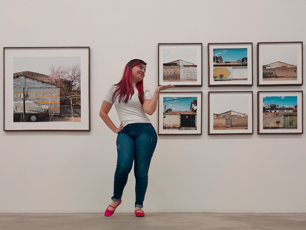 Uma foto minha, de cabelos cor de rosa, blusa branca, calça jeans e sapatos da mesma cor dos cabelos, em frente a duas obras de Jabulani. A primeira, uma fotografia de uma casa sul-africana. A segunda, o políptico de oitos obras já descrito anteriormente.