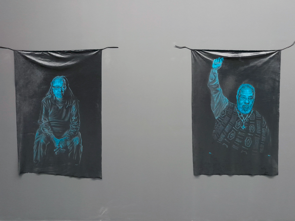 Duas das pinturas de tamanho médio, representando Sueli Carneiro, sentada apoiada em seus joelhos, e Abdias do Nascimento, em pé com o braços erguido.