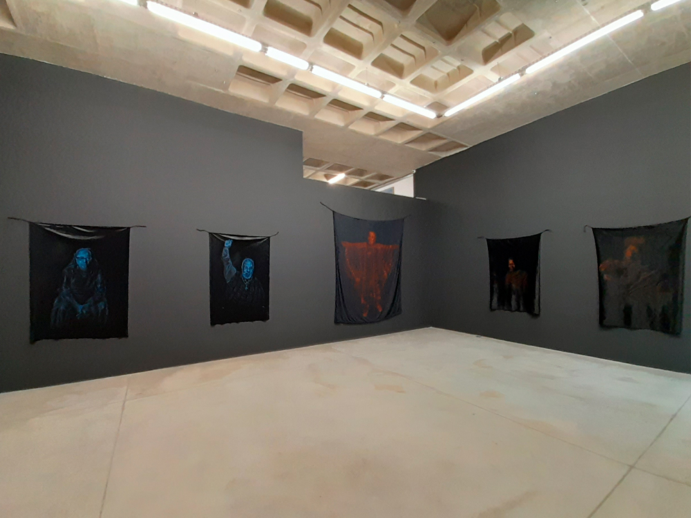 Outro ângulo da exposição com obras representando Sueli Carneiro, Abdias do Nascimento, Bispo do Rosário, Carolina Maria de Jesus e Conceição Evaristo, as duas primeiras em azul e as outras alaranjadas. A pintura do Bispo Tem grande formato.