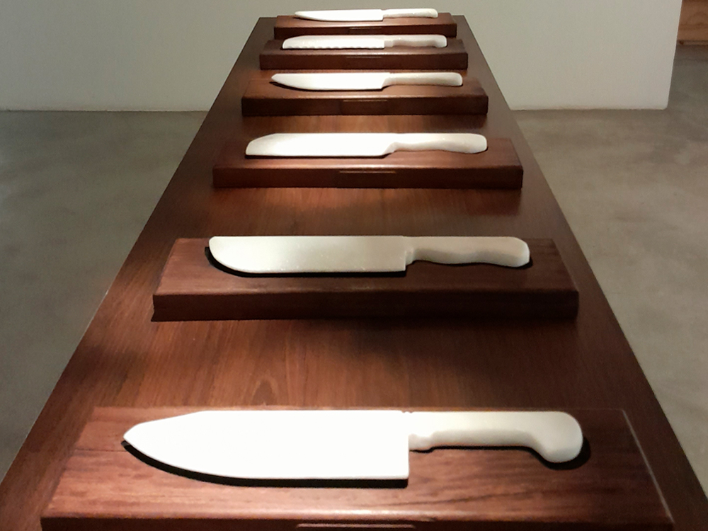 Mesa de madeira com a série Arma Branca de Marcel Diogo, um conjunto de seis facas de mármore com palavras gravadas.