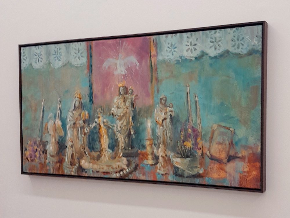 Pintura com tons suaves de azul, rosa e bege, representando um altar com várias esculturas de santos, velas e flores. No centro, uma figura com coroa segura uma criança, e acima delas há uma pomba branca sobre um fundo rosa, simbolizando o Espírito Santo.
