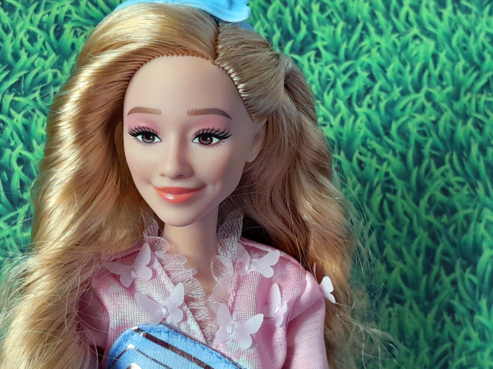 Close no rosto, destacando maquiagem suave, sorriso delicado e detalhes do cabelo loiro ondulado.