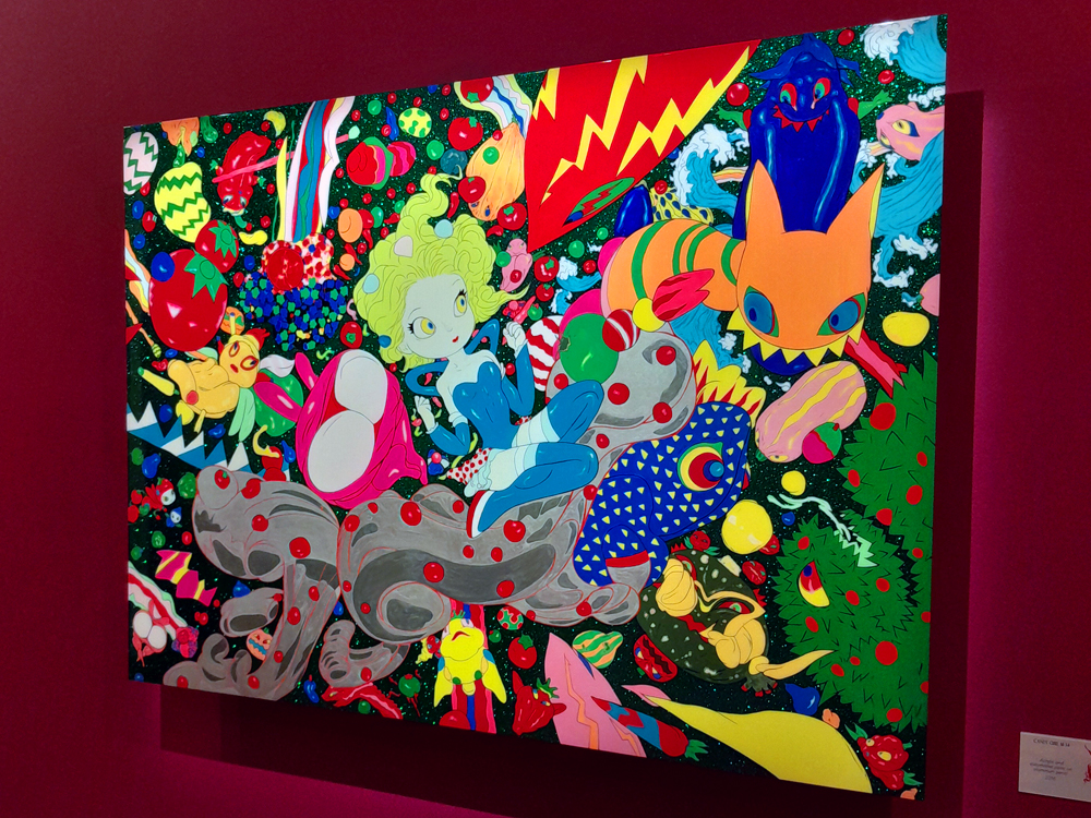 Grande pintura colorida com personagens fantásticos, criaturas e padrões vibrantes, exibida em parede rosa.