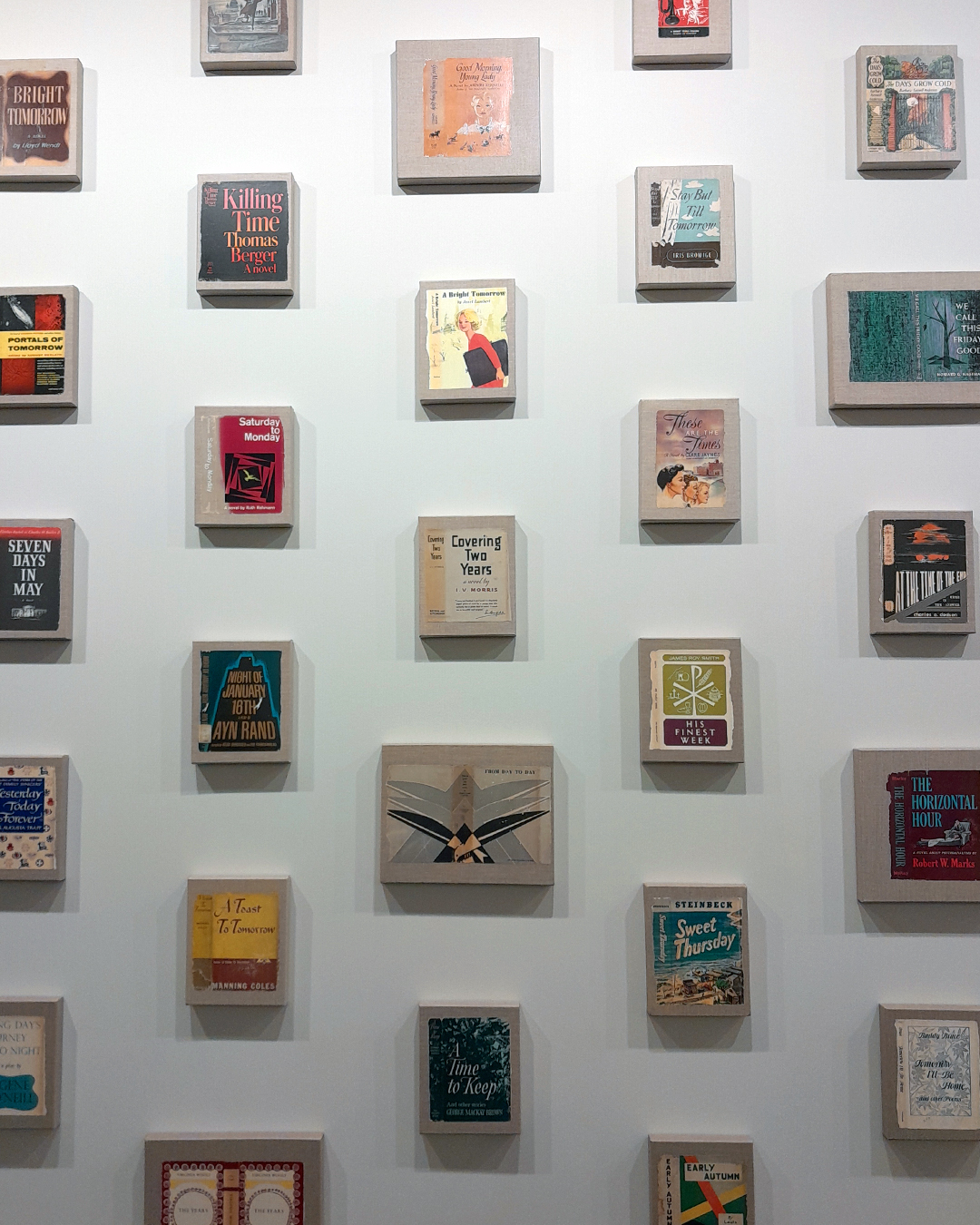 Instalação com livros expostos em uma parede branca, formando uma exposição de obras variadas, incluindo títulos de autores brasileiros e internacionais.