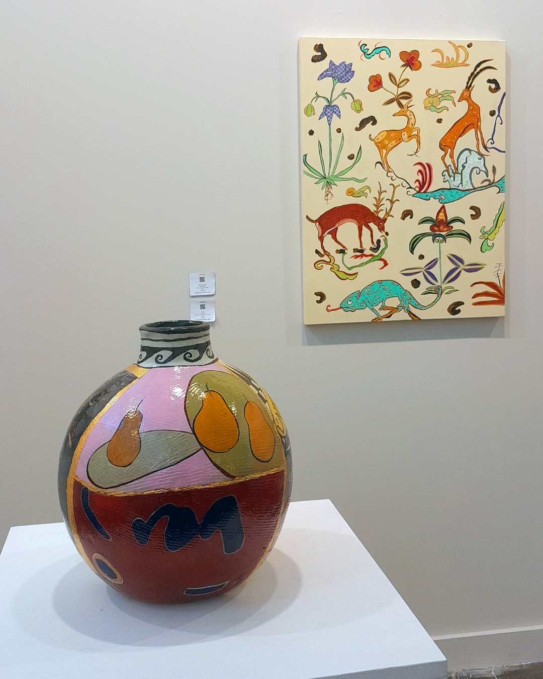 Duas obras coloridas, um vaso e uma pintura, que apresenta animais estilizados. A uma cerâmica vibrante está em primeiro plano.
