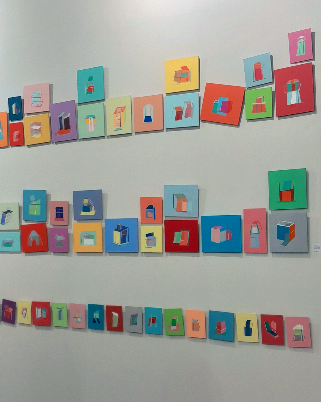 Composição colorida apresentando quadrinhos com diferentes objetos em um mural vibrante, organizados de maneira propositalmente na parede branca de um estande da SP-Arte.