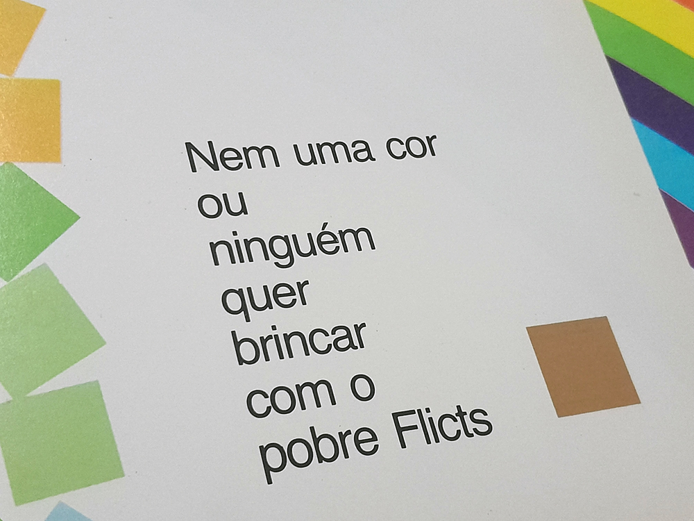 Página do livro onde se lê 'Nem uma cor ou ninguém quer brincar com o pobre Flicts' impressa em letras pretas sobre fundo branco. Ao redor do texto aparecem formas geométricas coloridas e, à direita, um pequeno quadrado na cor característica de Flicts, destacando o sentimento de exclusão abordado pela história.