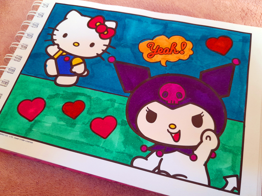 Página do livro de colorir mostrando Kuromi em primeiro plano sobre um fundo dividido entre azul e verde, decorado com corações vermelhos e um balão de fala escrito Yeah!. Ao fundo, Hello Kitty aparece observando a cena.