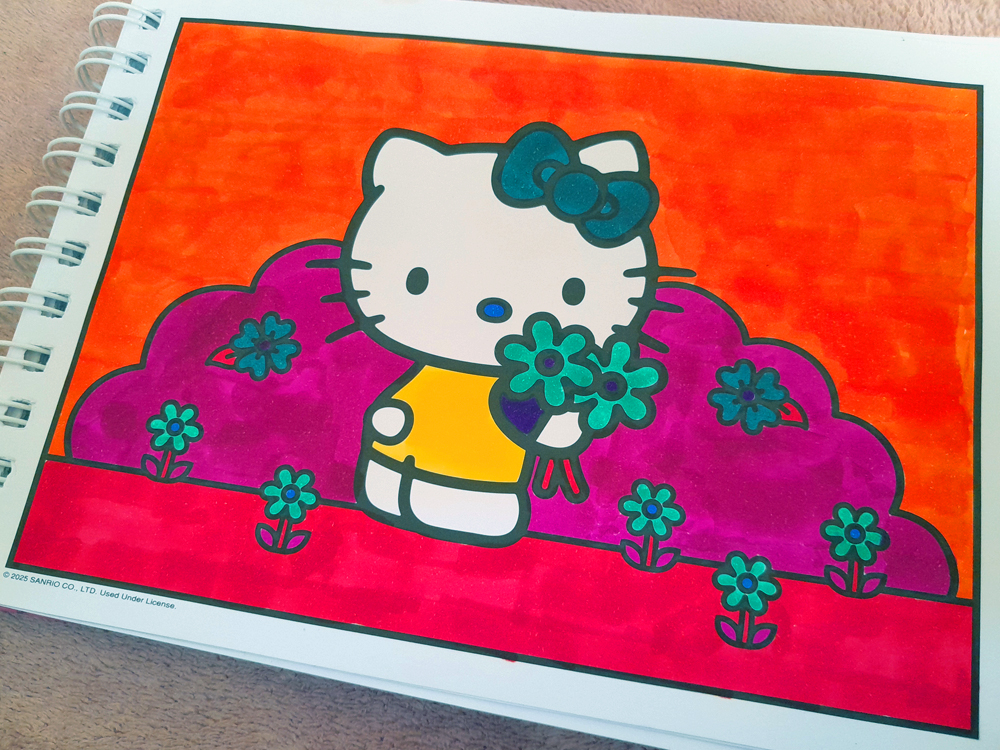 Ilustração da Hello Kitty segurando um buquê de flores azuis em um jardim estilizado. O céu foi colorido em laranja intenso, enquanto o chão aparece em rosa e os arbustos em tons de magenta, criando uma paleta vibrante e pouco convencional. As flores azul-turquesa contrastam com o restante da composição e evidenciam a experimentação com cores durante o processo de colorir.