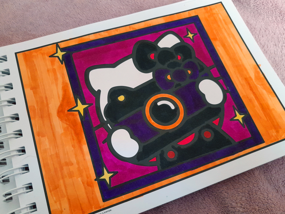 Página de livro de colorir da Hello Kitty, pintada com marcadores em cores vibrantes. Hello Kitty, Kuromi, Pompompurin e Keroppi aparecem em uma floresta diante de uma grande montanha, com árvores verdes, montanhas em tons de vermelho e laranja, céu azul intenso e algumas nuvens brancas.